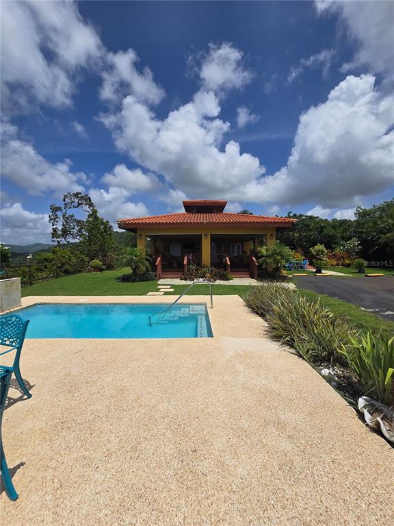 A swimming pool sits in front of a yellow house with a tiled roof — BO PULGUILLAS, CARR. 723, COAMO, PR