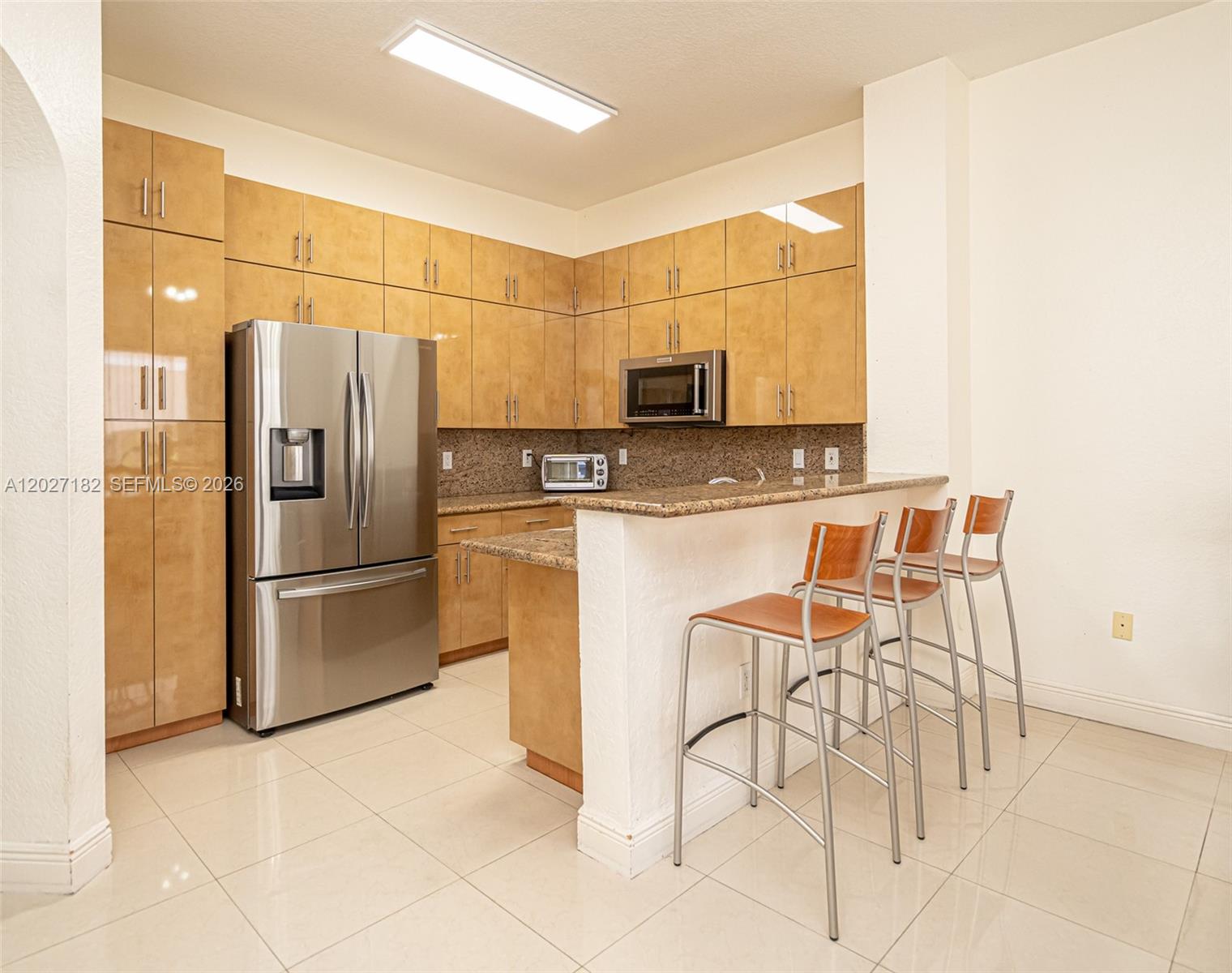 A kitchen features light wood cabinets, stainless steel appliances, granite countertops, and a breakfast bar — 14372 NW 83rd Ave, Miami Lakes FL 33016, MIAMI LAKES, FL