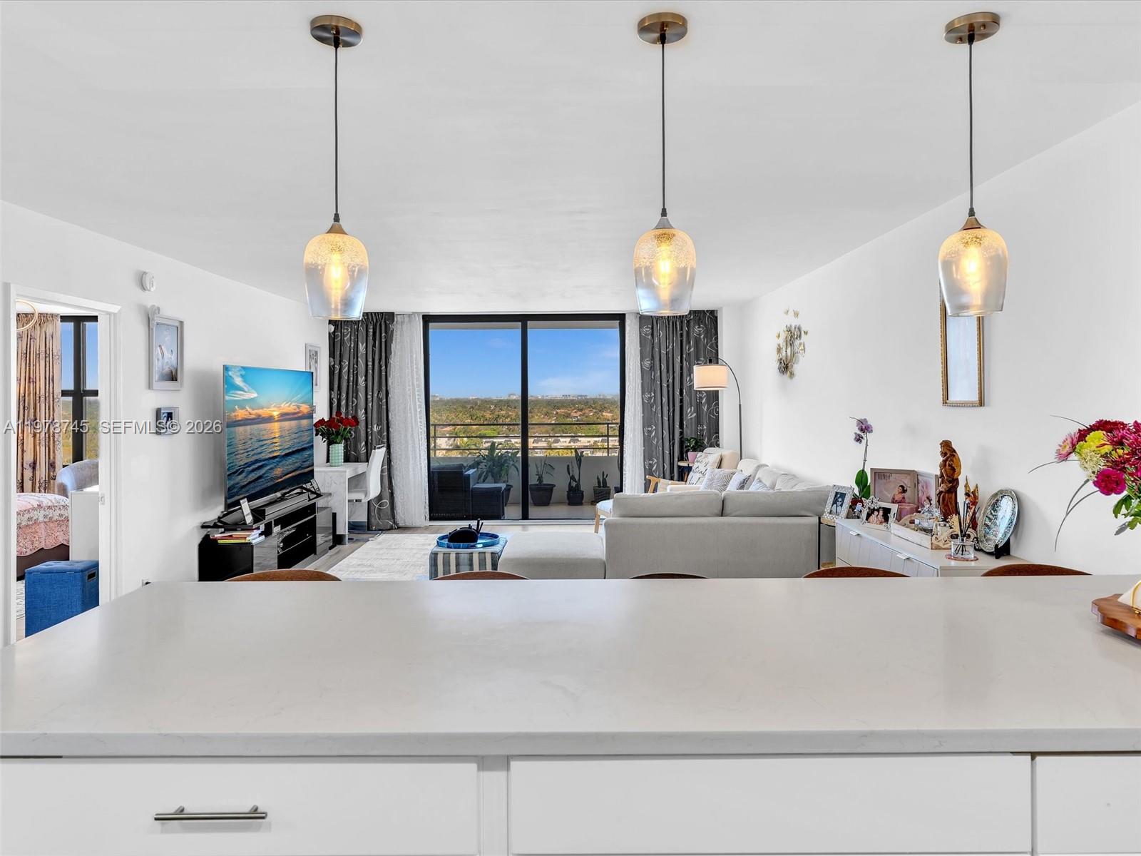 A kitchen island overlooks a living room with a television, sofa, and balcony view — 2500 Parkview Dr # 1108, Hallandale Beach FL 33009, HALLANDALE BEACH, FL