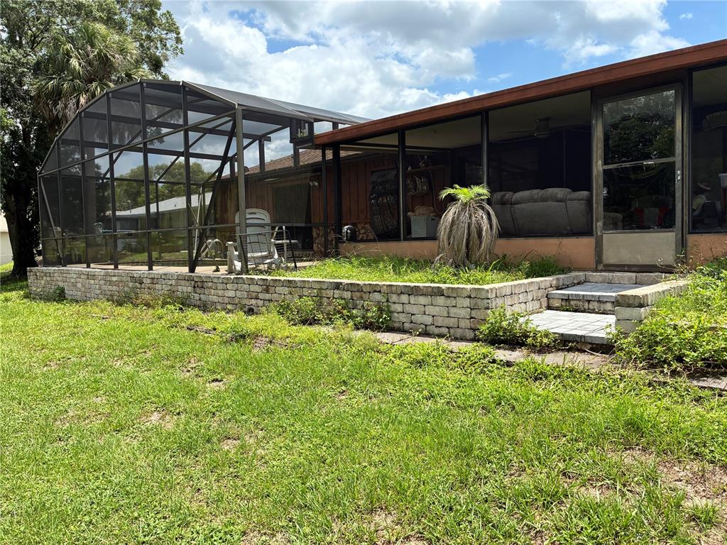 A screened-in patio with a brick retaining wall sits next to a house exterior — 1940 W NEMO DRIVE, DELTONA, FL