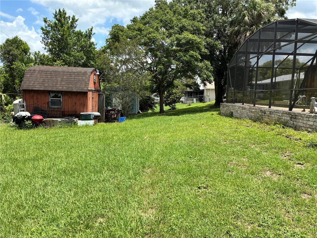 A grassy backyard features a wooden storage shed and a screened-in pool enclosure — 1940 W NEMO DRIVE, DELTONA, FL