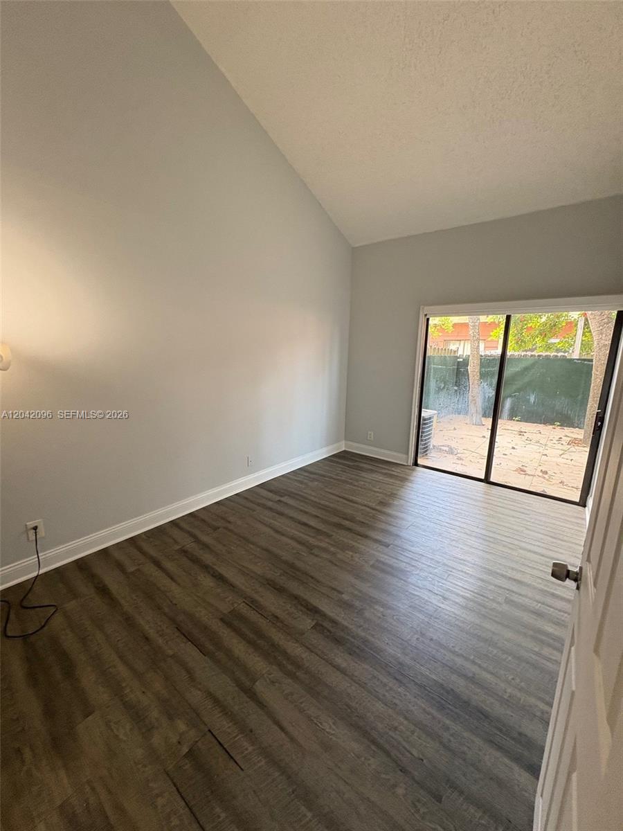 A room with vaulted ceilings, gray wood-look flooring, and a sliding glass door to a patio — 2309 NW 55th Ave, Lauderhill FL 33313, LAUDERHILL, FL