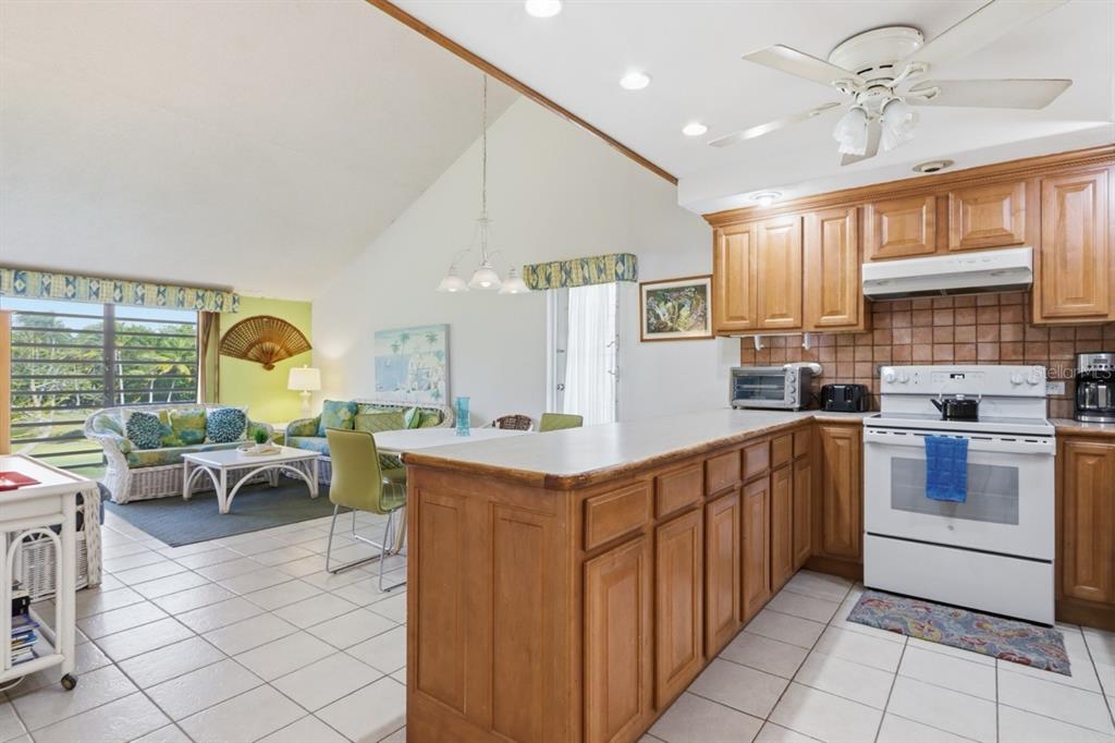 A kitchen with wood cabinets and a white stove opens into a living area — 1 BEACH VILLAGE DRIVE UNIT 92, HUMACAO, PR
