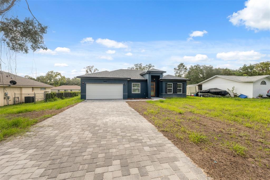A modern, dark-blue single-story house with a paved driveway and an unfinished grassy yard — 14152 SW 44TH AVENUE, OCALA, FL