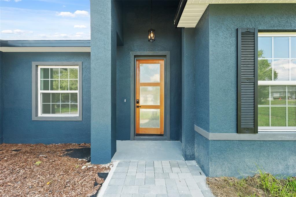 The exterior of a blue house features a wooden front door and a paved walkway — 14152 SW 44TH AVENUE, OCALA, FL