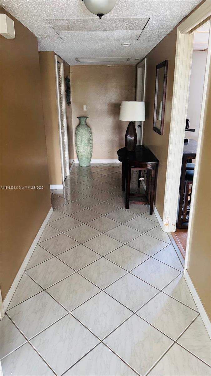 A hallway with light-colored diagonal floor tiles, tan walls, and a small wooden console table — 3150 N Palm Aire Dr # 801, Pompano Beach FL 33069, POMPANO BEACH, FL