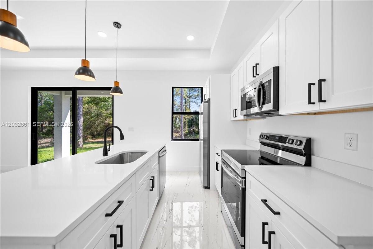A modern white kitchen features a central island, stainless steel appliances, and large sliding doors — 2609 53rd st w, Lehigh Acres FL 33971, LEHIGH ACRES, FL