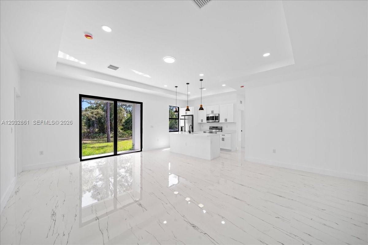 A bright, open-concept kitchen and living area features white marble floors and modern cabinetry — 2609 53rd st w, Lehigh Acres FL 33971, LEHIGH ACRES, FL