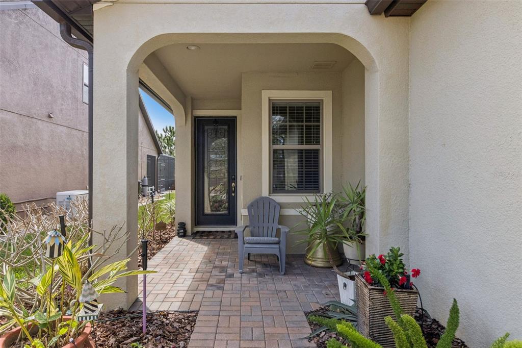 A covered entryway features a paved walkway, a gray Adirondack chair, and potted plants — 545 CANTABRIA DRIVE, DAVENPORT, FL