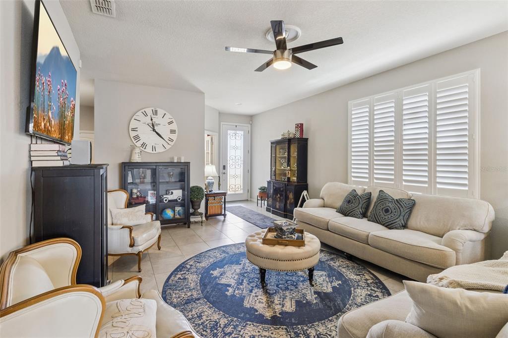 A living room features a round blue rug, beige sofa, armchairs, and a large wall clock — 545 CANTABRIA DRIVE, DAVENPORT, FL