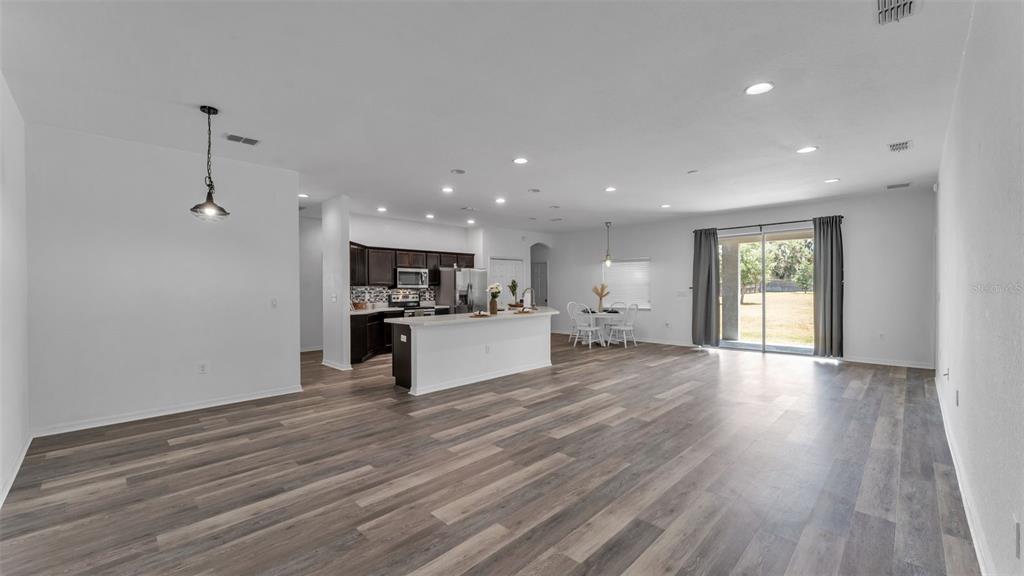 An open-concept kitchen and living area with wood-look flooring, white walls, and sliding glass doors — 119 GERBER DAIRY ROAD, EAGLE LAKE, FL