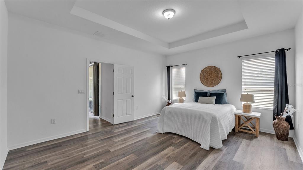 A bedroom features white walls, wood-look flooring, a tray ceiling, and a bed with nightstands — 119 GERBER DAIRY ROAD, EAGLE LAKE, FL