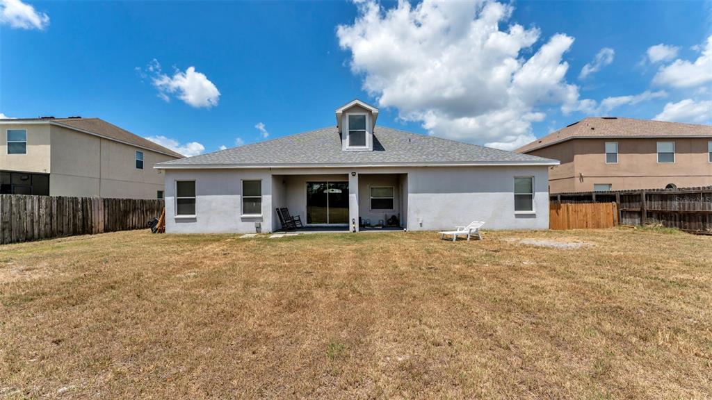 The rear exterior of a single-story house features a gray stucco facade and a yard — 119 GERBER DAIRY ROAD, EAGLE LAKE, FL