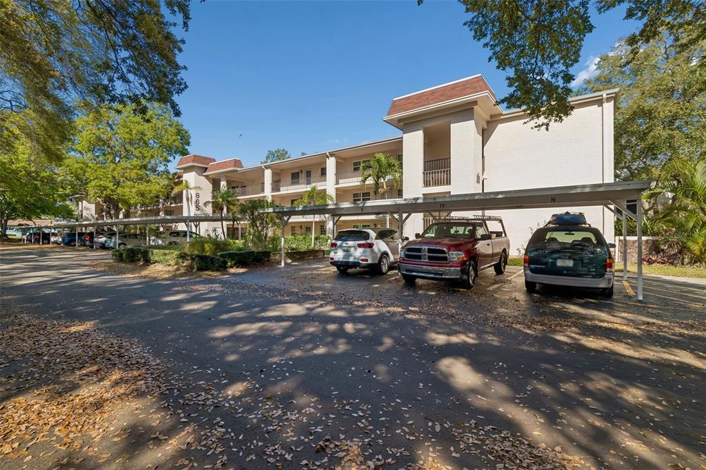 A multi-story apartment building with covered parking spaces and several cars in the foreground — 865 VIRGINIA COURT UNIT 108, DUNEDIN, FL