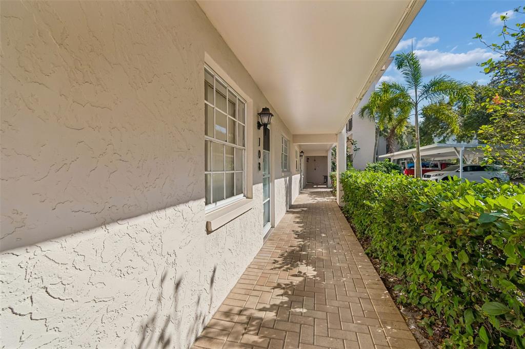 A paved walkway leads along the exterior of a stucco building with a covered porch — 865 VIRGINIA COURT UNIT 108, DUNEDIN, FL