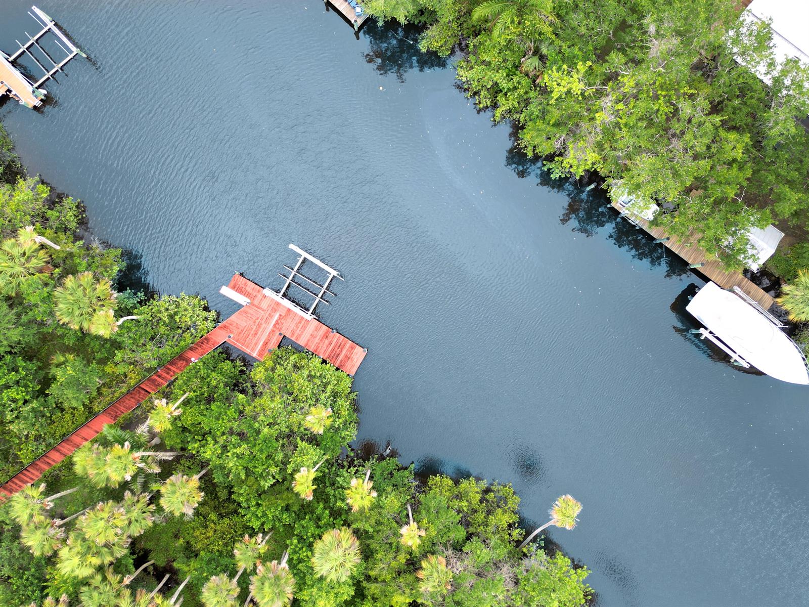 An aerial view shows a wooden dock extending into a narrow canal lined with trees — 299 SW Lost River Road, Stuart FL 34997, STUART, FL