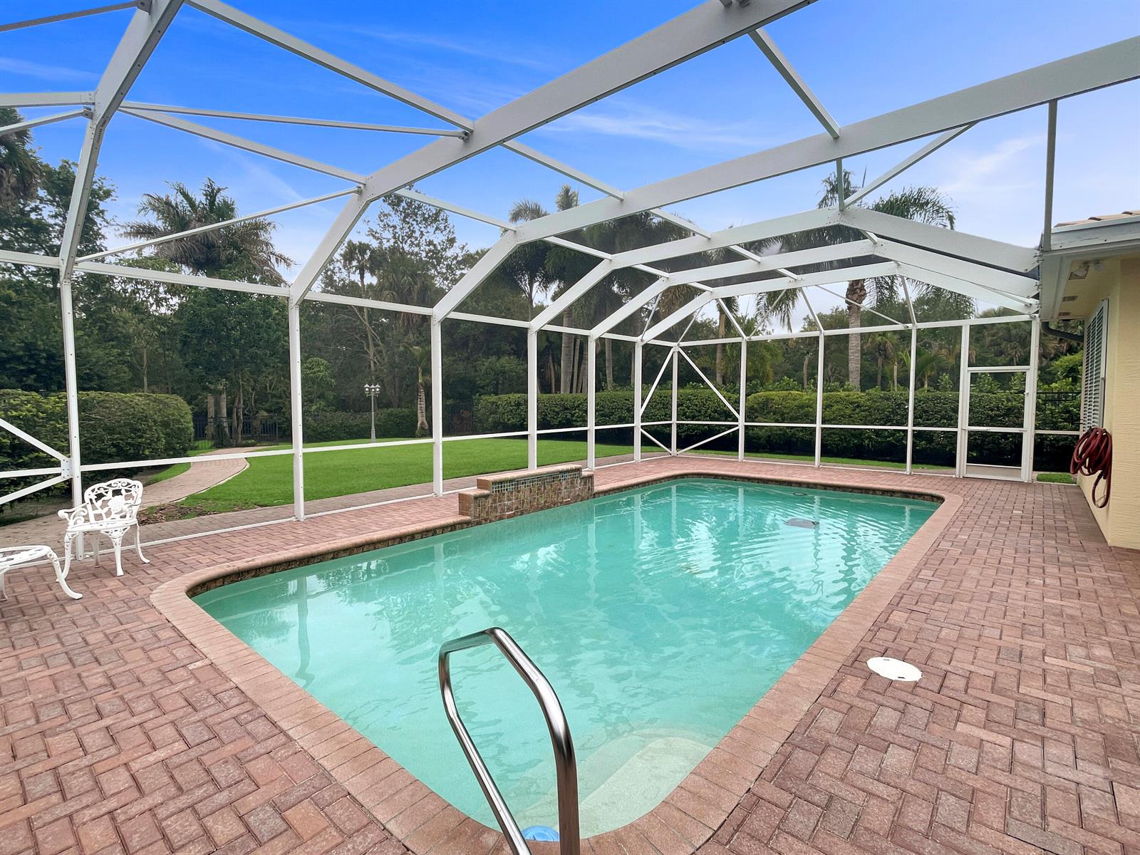 A swimming pool with a brick deck is enclosed by a white metal screen cage — 299 SW Lost River Road, Stuart FL 34997, STUART, FL