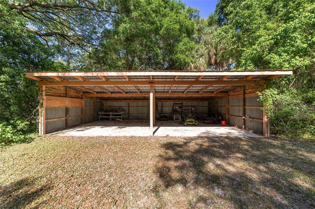 A metal-roofed, open-sided pole barn with a concrete floor sits in a wooded area — 14020 NW 160TH AVENUE, WILLISTON, FL