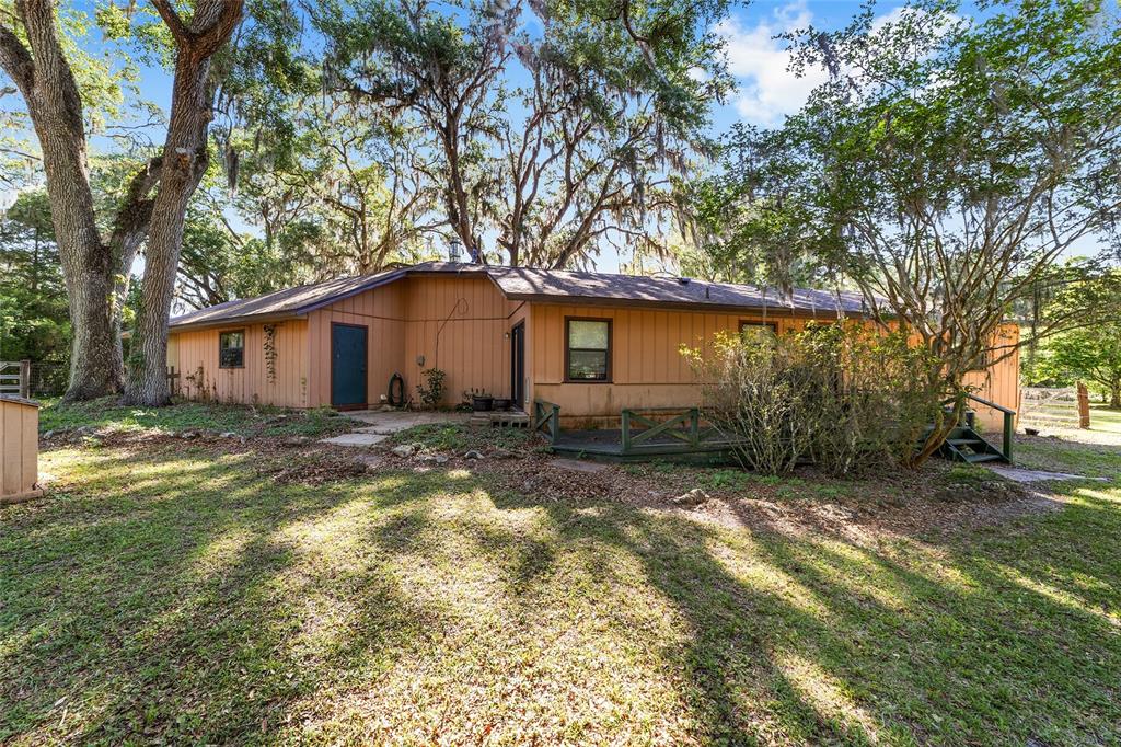 A single-story house with tan vertical siding, a dark roof, and a wooden deck — 14020 NW 160TH AVENUE, WILLISTON, FL