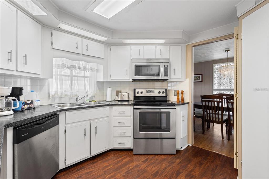 A kitchen with white cabinets, stainless steel appliances, dark countertops, and wood-look flooring — 2100 KINGS HIGHWAY UNIT 175, PORT CHARLOTTE, FL
