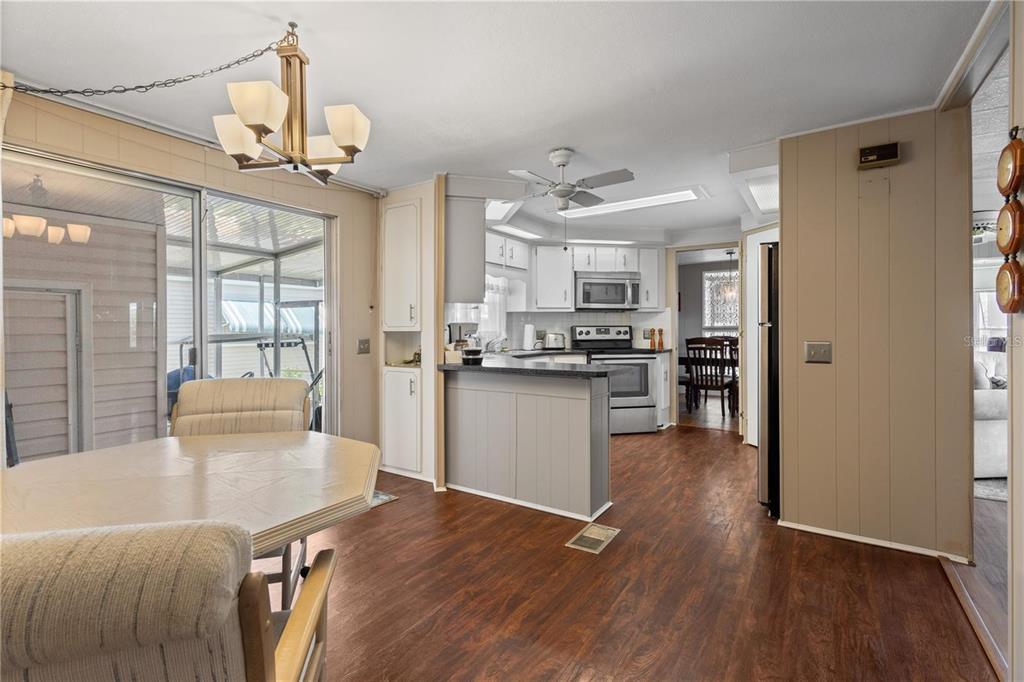 A dining area with wood-look flooring leads into a kitchen featuring white cabinets and appliances — 2100 KINGS HIGHWAY UNIT 175, PORT CHARLOTTE, FL