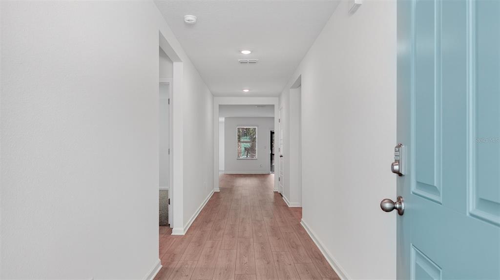 A view from an open blue front door into a hallway with wood-look flooring — 29 SAWDUST LANE, PALM COAST, FL