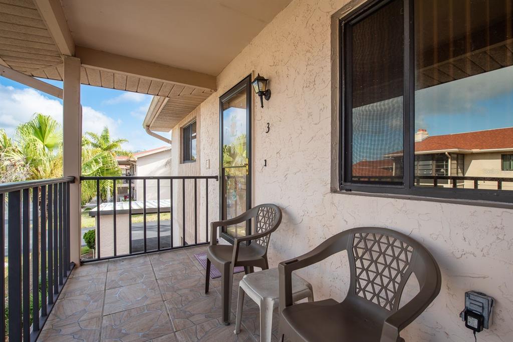 A covered balcony features tiled flooring, two plastic chairs, a small table, and a screen door — 9910 EAGLES POINT CIRCLE UNIT 3, PORT RICHEY, FL