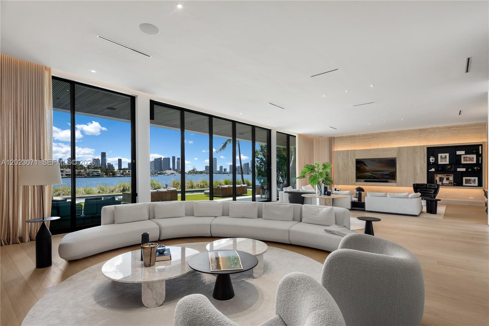 A spacious living room features a curved white sofa, marble coffee tables, and floor-to-ceiling windows — 28 W Dilido Dr, Miami Beach FL 33139, MIAMI BEACH, FL
