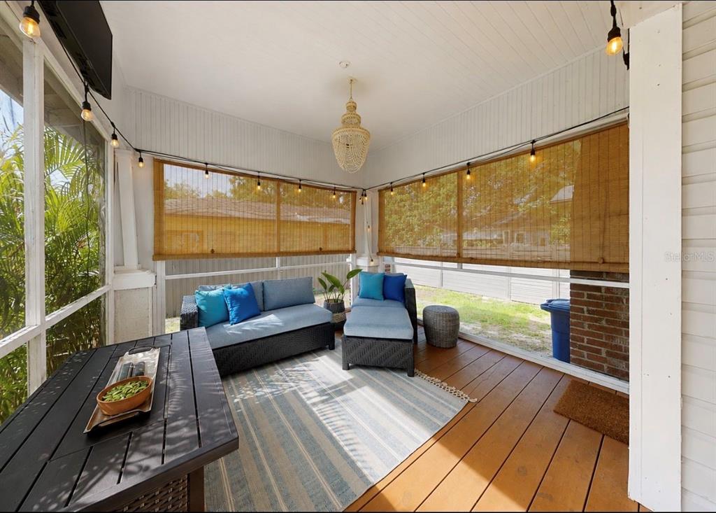 A screened-in porch features wicker furniture, a fire pit table, and string lights — 6702 N ELIZABETH STREET, TAMPA, FL