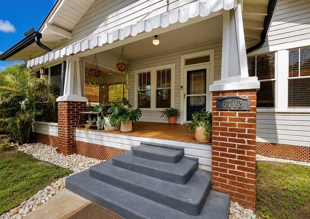 A covered wooden porch features gray siding, large windows, and several potted plants — 6702 N ELIZABETH STREET, TAMPA, FL