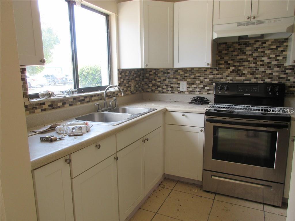 A kitchen features white cabinets, a stainless steel stove, and a mosaic tile backsplash — 111 MICHELLE LANE UNIT B, KISSIMMEE, FL