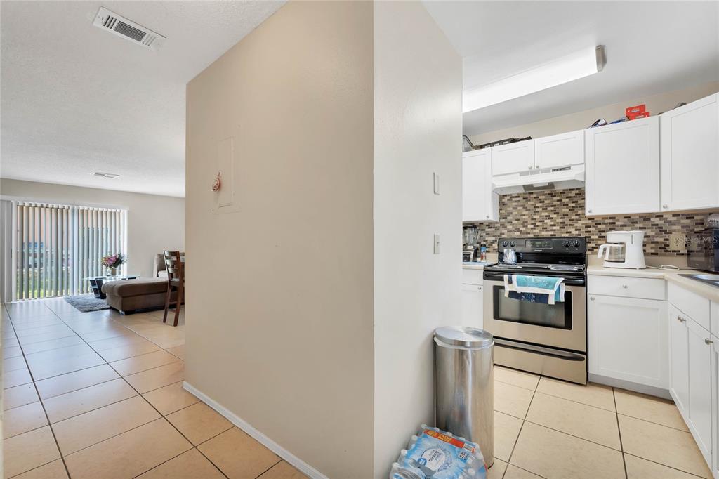 A kitchen with white cabinets and stainless steel appliances opens to a tiled living area — 111 MICHELLE LANE UNIT B, KISSIMMEE, FL