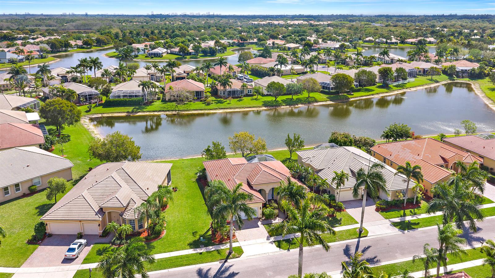 An aerial view shows a suburban neighborhood with houses surrounding a central lake — 9531 Lantern Bay Circle, West Palm Beach FL 33411, WEST PALM BEACH, FL