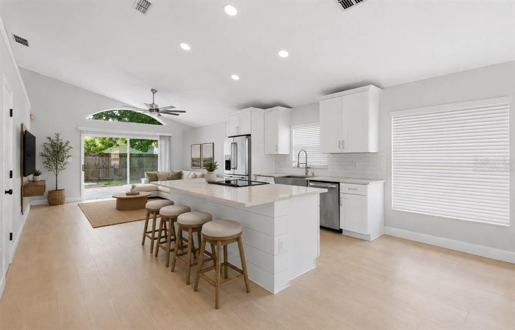 A bright kitchen and living area with white cabinets, a central island, and sliding doors — 1960 AQUARIUS COURT, OVIEDO, FL