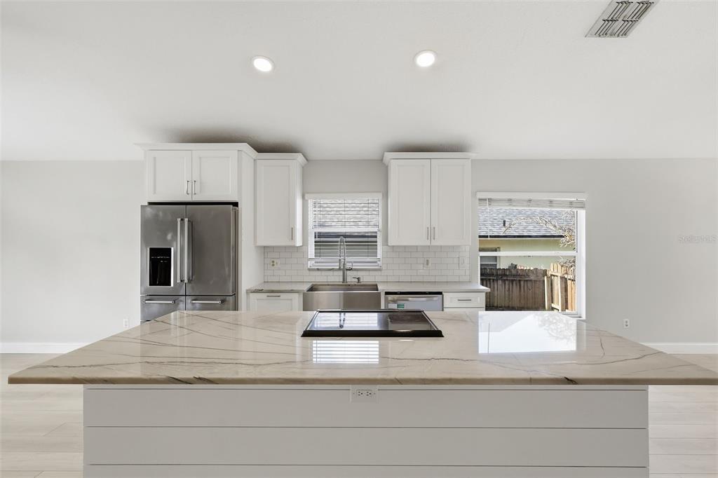 A kitchen features a large island with a cooktop, white cabinets, and stainless steel appliances — 1960 AQUARIUS COURT, OVIEDO, FL