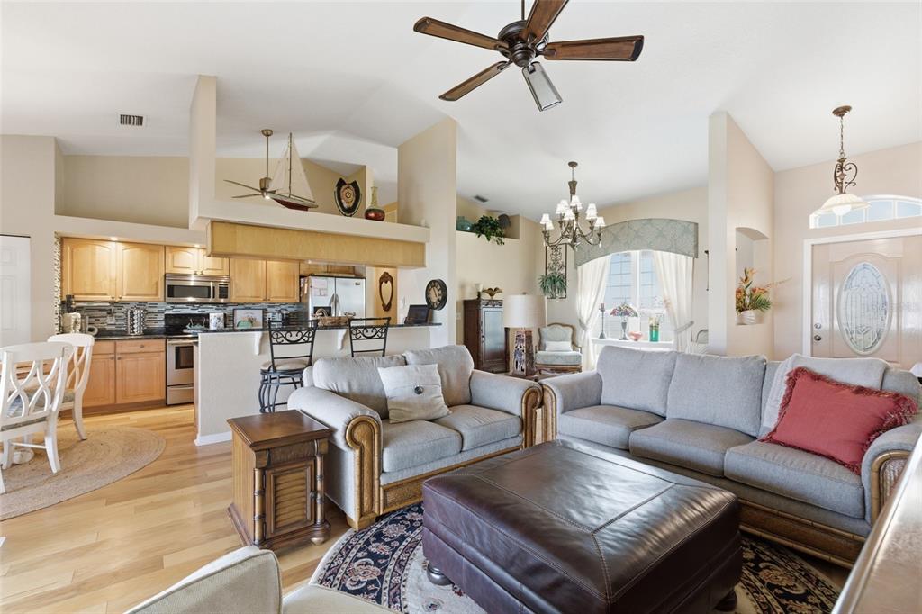 An open-concept living room and kitchen feature light wood cabinetry, neutral furniture, and vaulted ceilings — 1318 PENGUIN COURT, PUNTA GORDA, FL