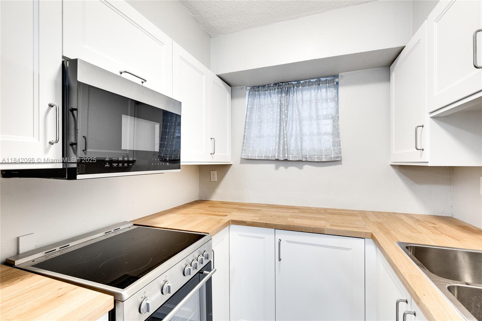 A small kitchen features white cabinets, a wood countertop, and a stainless steel stove — 2465 SW 18th Avenue # 3208, Miami FL 33145, MIAMI, FL