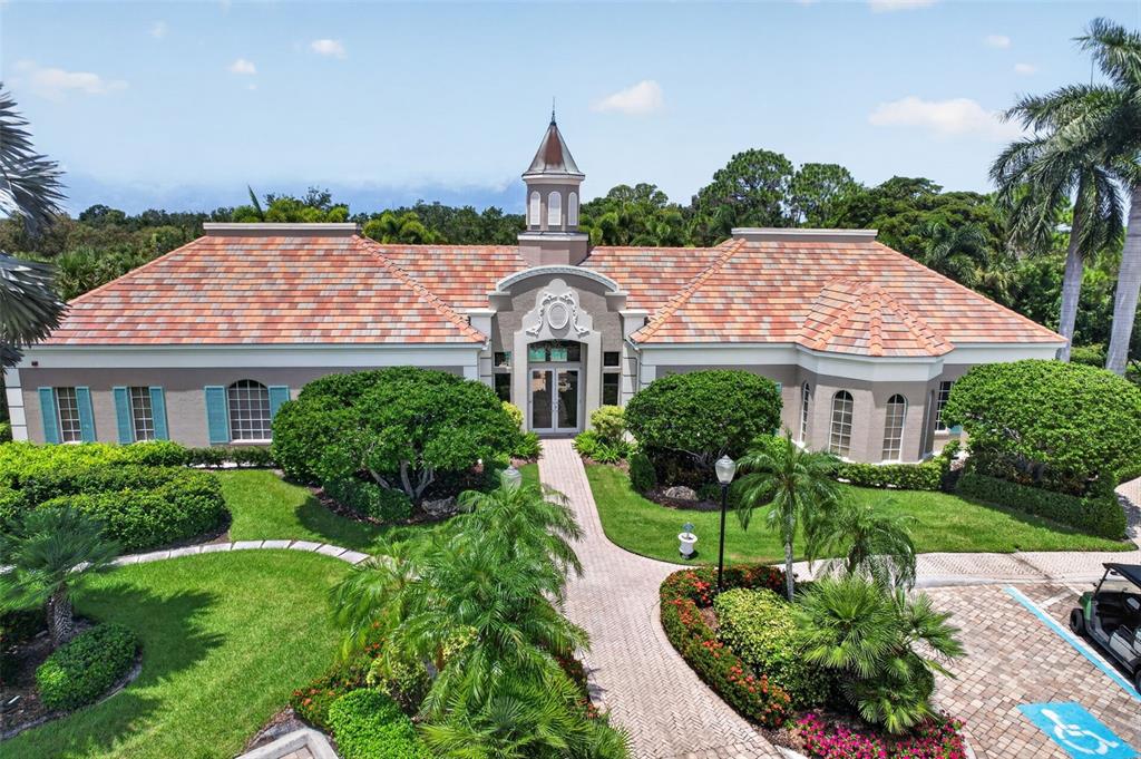 An exterior view of a single-story building with a tiled roof, cupola, and landscaped grounds — 7492 BOTANICA PARKWAY UNIT 102, SARASOTA, FL