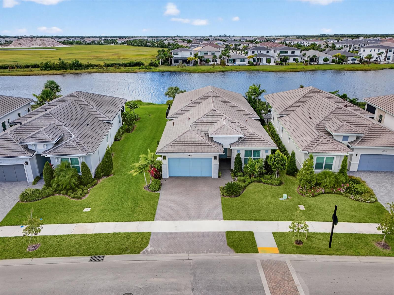 A covered patio with brick pavers overlooks a backyard putting green, lake, and blue sky — 10033 Regency Way, Palm Beach Gardens FL 33412, PALM BEACH GARDENS, FL