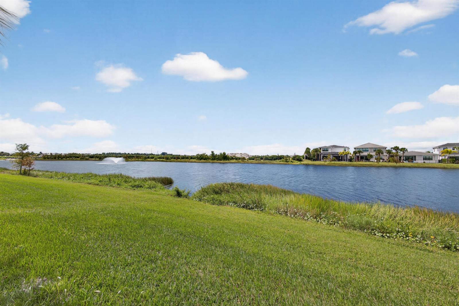 A grassy lawn overlooks a lake with a fountain and houses in the distance — 10033 Regency Way, Palm Beach Gardens FL 33412, PALM BEACH GARDENS, FL