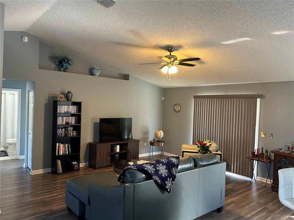 A living room features a vaulted ceiling, a ceiling fan, a television, and wood flooring — 4 LYSANDER LANE, PALM COAST, FL