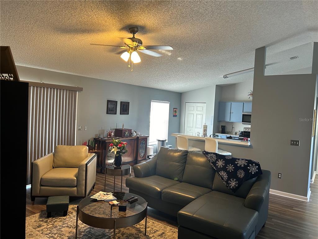 A living room with a gray sectional sofa, an armchair, and an open kitchen area — 4 LYSANDER LANE, PALM COAST, FL