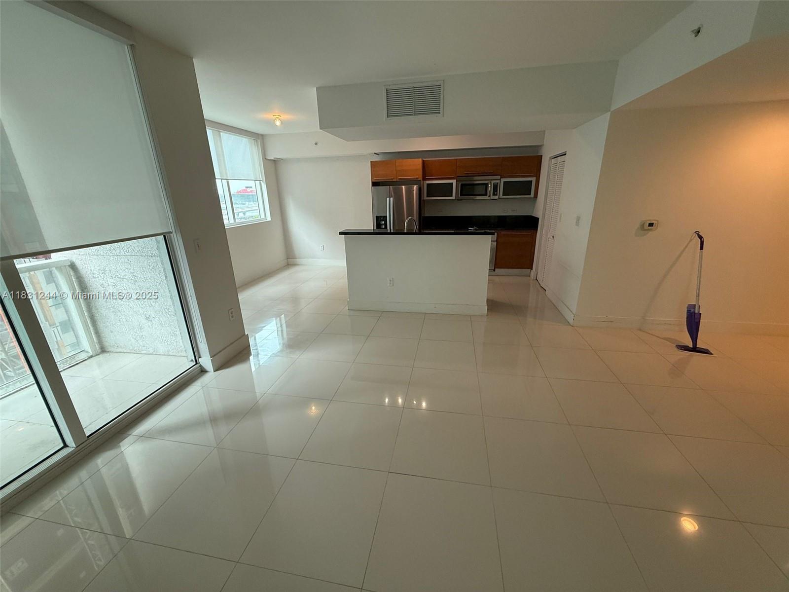 An open-concept kitchen with wood cabinets and white tile floors overlooks a living area — 244 Biscayne Blvd # 908, Miami FL 33132, MIAMI, FL