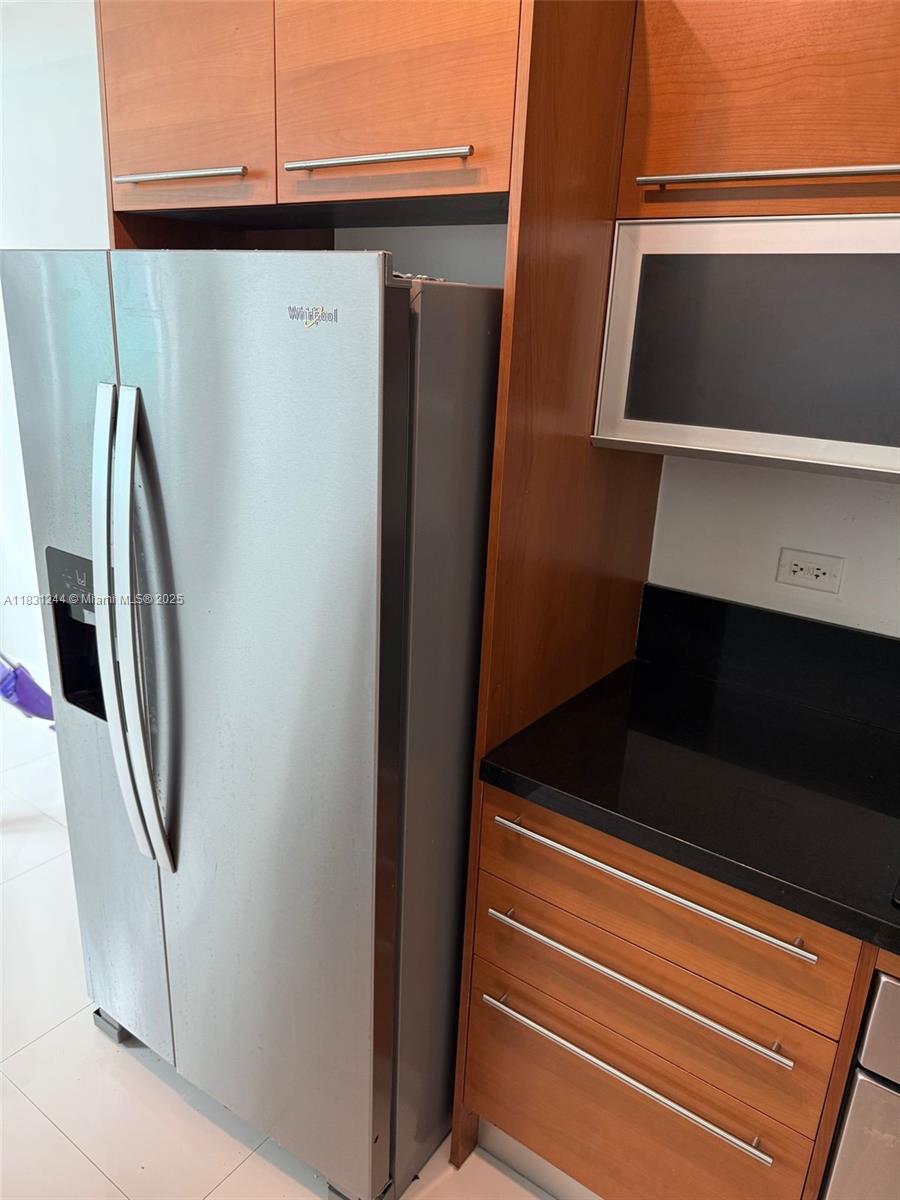 A stainless steel refrigerator stands next to wood cabinets and a black countertop — 244 Biscayne Blvd # 908, Miami FL 33132, MIAMI, FL