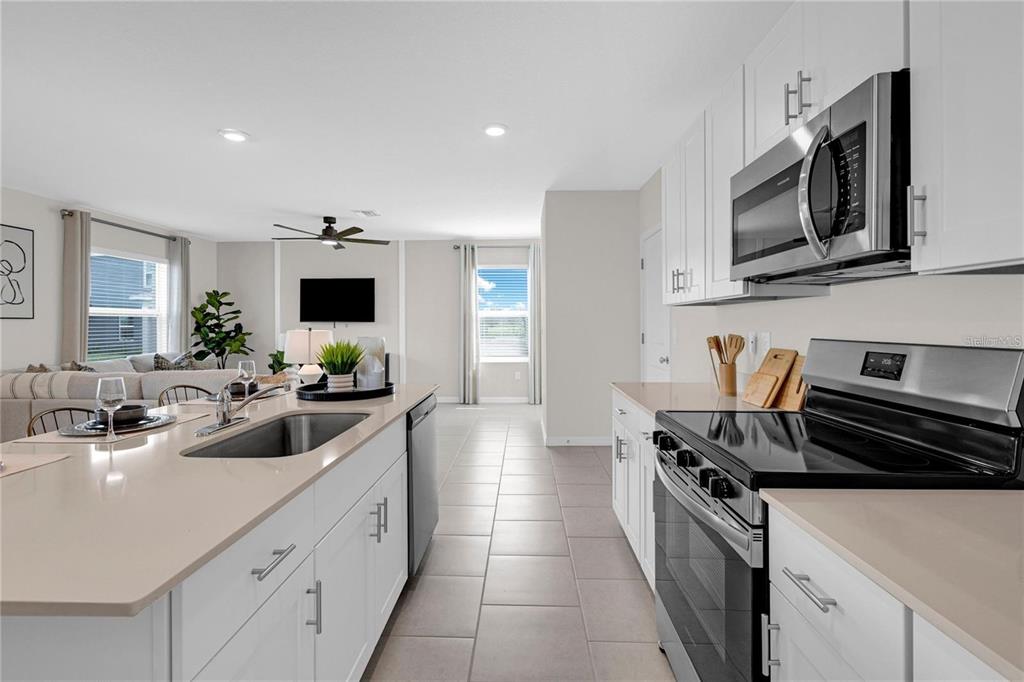 A modern kitchen with white cabinets and a quartz island overlooks an open living area — 13239 TURNLEAF BOULEVARD, PUNTA GORDA, FL