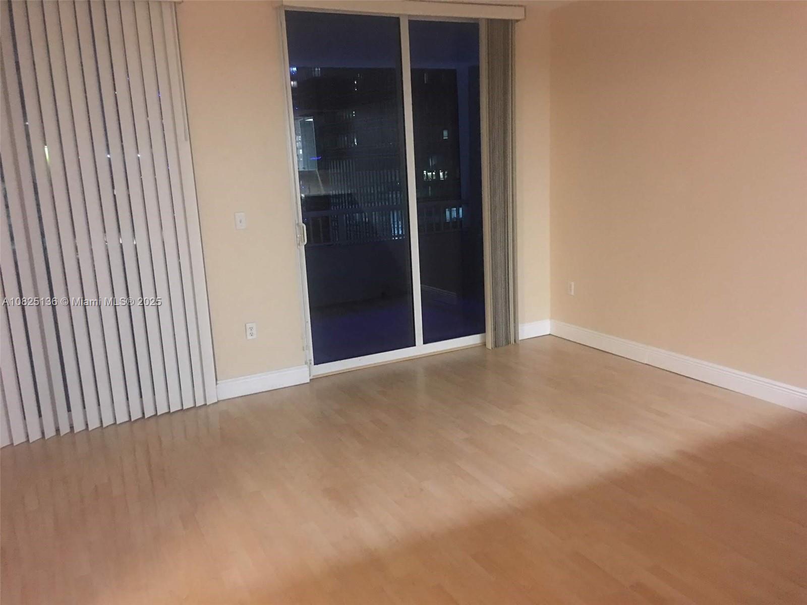 An empty room features light wood flooring, beige walls, and a sliding glass balcony door — 170 SE 14th St # 1407, Miami FL 33131, MIAMI, FL