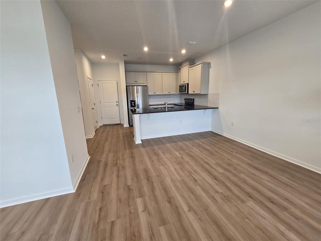 A kitchen with white cabinets and a black countertop overlooks an open-concept living area — 7774 CLOVE HITCH WAY, ORLANDO, FL