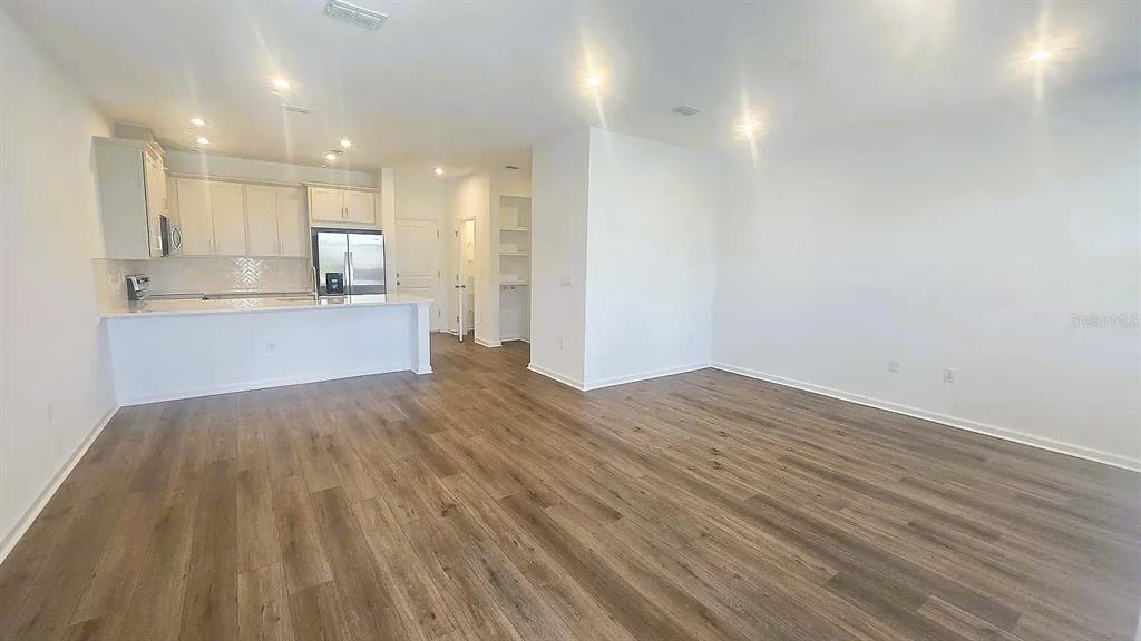 An open-concept kitchen with white cabinets and a breakfast bar overlooks a spacious living area — 7774 CLOVE HITCH WAY, ORLANDO, FL