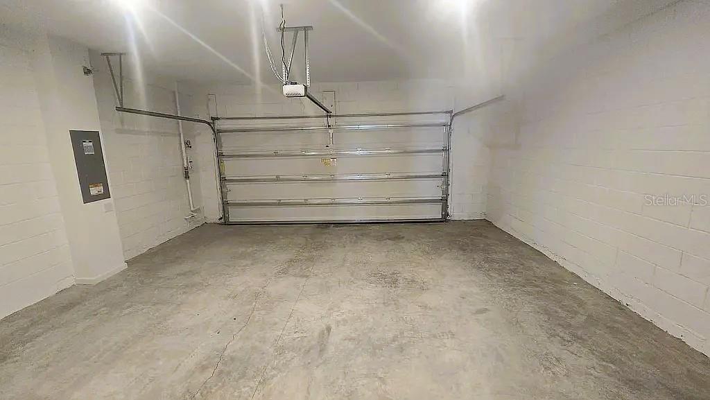 An empty garage with a concrete floor, white block walls, and a metal sectional door — 7774 CLOVE HITCH WAY, ORLANDO, FL