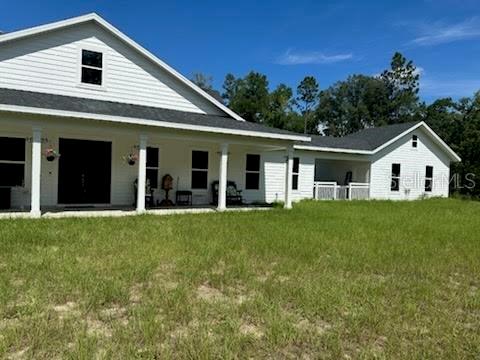 A white farmhouse with a large covered porch sits on a grassy lot — 5040 NE 48TH COURT, HIGH SPRINGS, FL